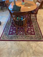 Rectangular red and beige rug under a wooden dining table with floral garland pattern visible around edges.