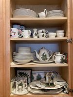 Cabinet shelves showing stacked dinner plates, salad plates, mugs, teapot, sugar pot and tree-pattern dinnerware
