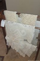 Doilies draped over a wooden rack showing multiple crocheted pieces of various patterns and sizes.