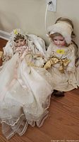 Wide view showing both dolls seated on floor, dressed in lace and bonnet, porcelain craftsmanship