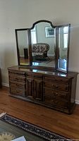 Front view of dresser with tri-fold mirror attached showing nine drawers and central cabinet doors with brass handles.