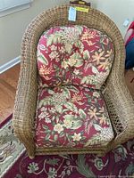 Full view of faux wicker arm chair with floral cushions on a patterned rug near a window.