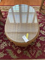 Top view of oval faux wicker coffee table with clear glass top and carpet beneath.