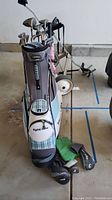 Full view of Adams Tight Lies stand bag with clubs, head covers on floor and cart behind