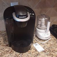 Photo of black Keurig coffee maker and white Cuisinart Mini Prep Plus food processor side by side on countertop.