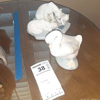 Photo showing the swan and polar bear Lladro figurines on glass table with MaxSold auction tag visible
