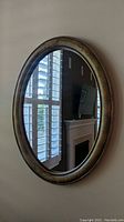 Oval wall mirror with painted distressed frame, mounted on beige wall, reflecting the room interior.