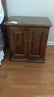 Front view of dark wood Ethan Allen nightstand with double doors and brass handles on hardwood floor beside bed.