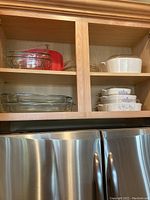 Wide view of upper and lower cabinet showing stacked clear glass bakeware and Corningware pieces, demonstrating full lot content