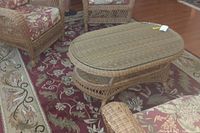 Photo showing Central Oriental area rug under wicker furniture, highlighting burgundy and beige floral design, with coffee table on top.