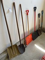 Full view of all seven tools leaning against a wall including 3 shovels, pitchfork, rake, and 2 snow shovels
