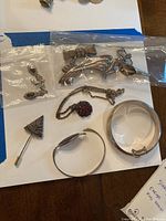 Full lot overview including earrings in plastic bag, multiple brooches, bracelets, hat pin, and necklace with pendant on a white surface with blue tape background