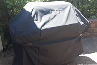 Grill covered by black nylon Weber cover outdoors