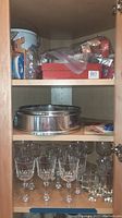 Wine glasses, springform pan on middle shelf, cookie cutters and cupcake molds on top shelf inside wood cabinet.