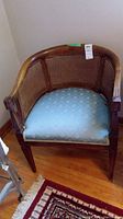 Full view of wood framed chair, showing rounded cane back and sides, and blue upholstered seat on hardwood floor.