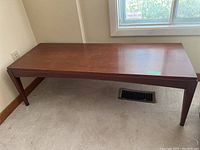 Full side view of rectangular wood coffee table, showing simple legs and reddish-brown finish.
