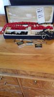 Photo showing the open box with red bead necklaces, black bead earrings, and a box containing earring backs. Shows the range of costume jewelry in lot.