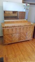 Full frontal view of the wooden dresser with the attached rectangular mirror above, both medium-tone wood with geometric veneer pattern on drawer fronts and metal knobs.