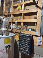 Full view of two wall-mounted blue plastic multi-drawer organizers and wooden shelves stored in basement furnace room near water heater. Shows placement and variety of stored hardware supplies.