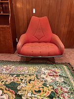 Front view of mid-century modern upholstered easy chair with orange-red fabric and visible wear. Wood frame base partially covered with duct tape.
