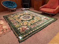 Wide view of the vintage velour rug or throw laid on carpeted floor surrounded by furniture including a blue cushioned chair and an orange chair.