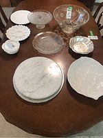 Wide shot showing full set of servingware on wooden table including crystal bowl, ceramic dishes, silverplated bowl, marble plates, and glass cake stand.