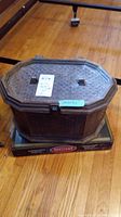 Exterior view of vintage octagonal woven sewing basket with lid and latch closure, placed on wooden floor.