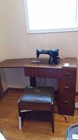 Full view of Singer sewing machine mounted on wooden desk with accompanying wooden stool in foreground