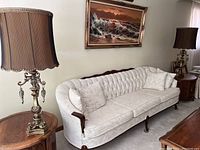 Pair of ornate table lamps with pleated shades on a round wooden table next to a white upholstered sofa.