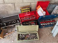 Multiple toolboxes and assorted tools arranged against a concrete block wall including red, blue, black and green cases