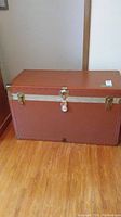 Front view of the brown metal trunk with latch and lock showing overall condition and size.
