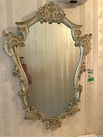 Full view of the wall mirror showing the ornate, gold-toned carved frame and reflective glass.