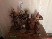 Photo showing six figurines including wood carvings and papier-mâché figures arranged on a wooden surface against wallpaper