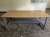 Full view of rectangular cork top table on metal frame with lower shelf, shown in a room with carpet flooring