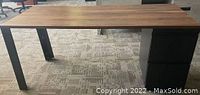 Front facing photo of wooden office desk with black metal legs and attached black two-drawer filing cabinet on right side.