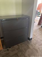 Gray 3-drawer filing cabinet with lock, showing full front and side view in office setting