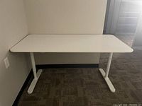 White office table with rounded edges and white metal legs, in an office corner.