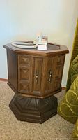 Wooden octagonal bedside table with paneled doors and dark inset top holding a white corded telephone.