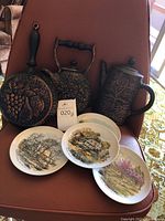 3 decorative painted ceramic plates with rural themes, 1 decorative ceramic teapot with grapevine pattern, 1 hanging decorative frying pan, and 1 hanging decorative kettle with grapevine pattern