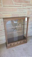 Front and partial side view of the wood and glass display cabinet against a brick wall.