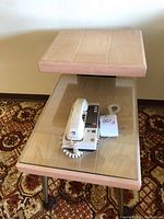 Front view of vintage end table showing wood top tier and glass top lower tier with vintage corded telephone on it.