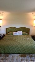 Full front view of king size bed with green tufted velvet headboard, green quilted comforter, and two decorative pillows.