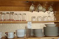 Shelves with an assortment of glasses, wine glasses, coffee mugs hanging by hooks, bowls, and plates stacked underneath.