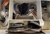Top view of assorted pots, pans, lids and baking sheets stacked inside a drawer.