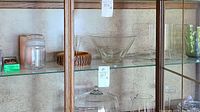 Photo of glass nut bowl with wooden base, glass pitcher, bowl and serving platter inside a wooden and glass cabinet