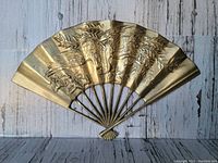 Front view of brass fan wall decor showing detailed embossing of bird and leaves