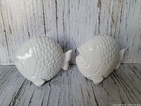 Two white ceramic fish salt and pepper shakers on a rustic wooden surface, showing their side profiles and scale texture.