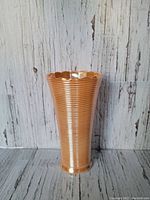 Front side view of the peach-colored Fire King flower vase showing its ribbed texture and scalloped rim.