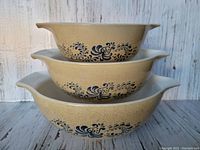 Stacked side view of the three nested Pyrex Homestead bowls showing blue floral pattern and beige exterior.