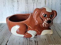 Front and left side view of brown and white ceramic dog-shaped planter with a hollow back for planting, showing detailed face with black eyes and white dots.